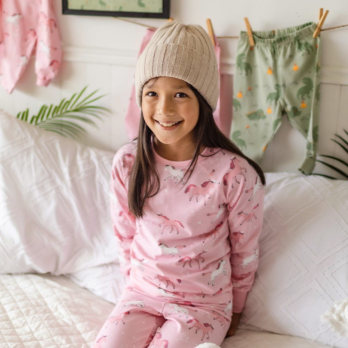 Fille portant un pyjama rose en coton à motifs de licornes Souris Mini, confortablement assise sur un lit douillet.