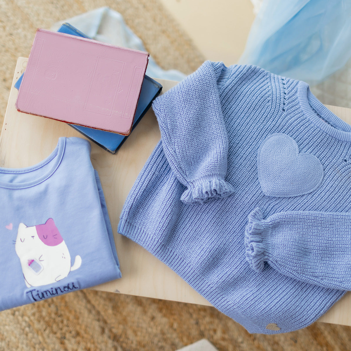 T-shirt bleu avec illustration de chat pour bébé à manches longues, présenté plié à côté d'un chandail de maille bleu avec cœur.
