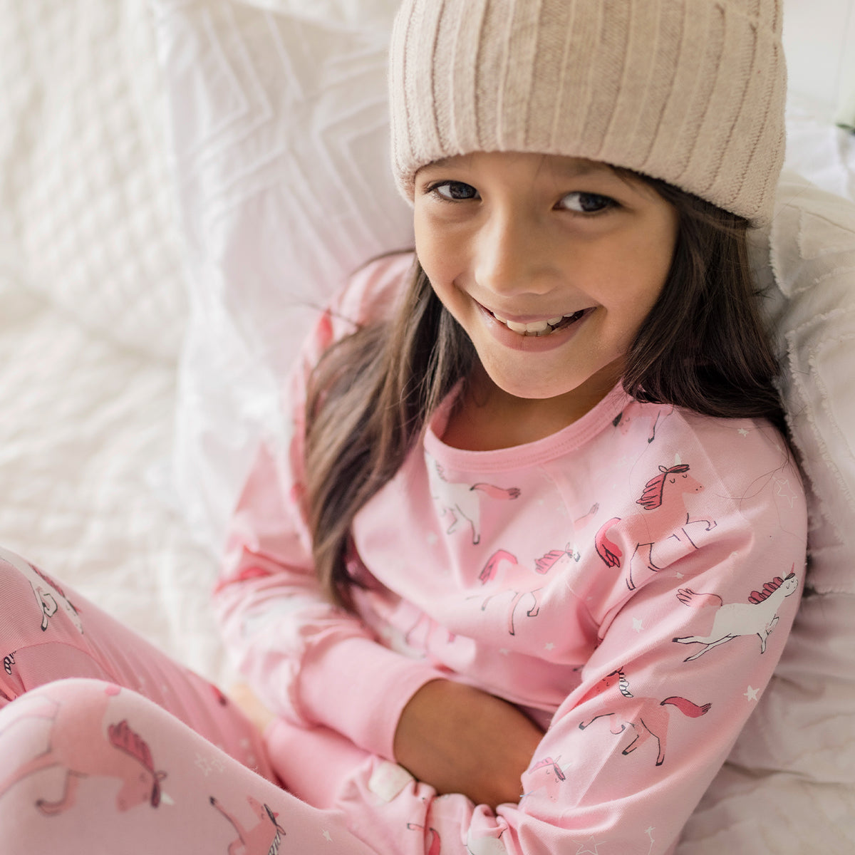 Fille portant un pyjama rose en coton à motifs de licornes Souris Mini, confortablement assise sur un lit douillet.