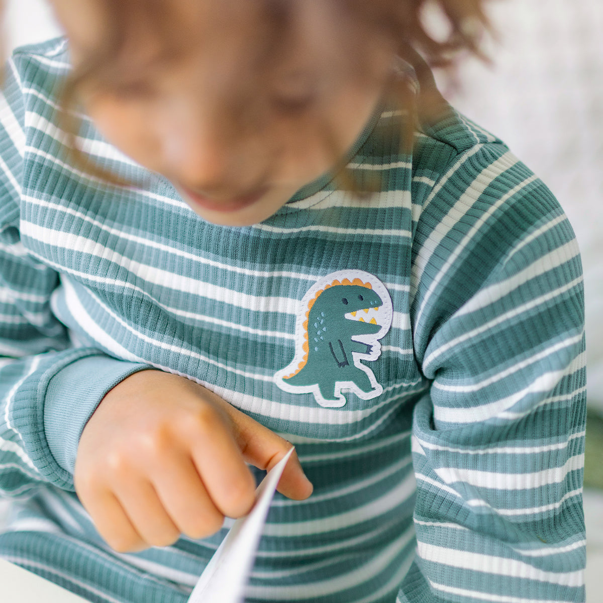 Gros plan du pyjama deux pièces vert à rayures pour enfant en coton côtelé, porté par un enfant et orné d'un écusson de dinosaure