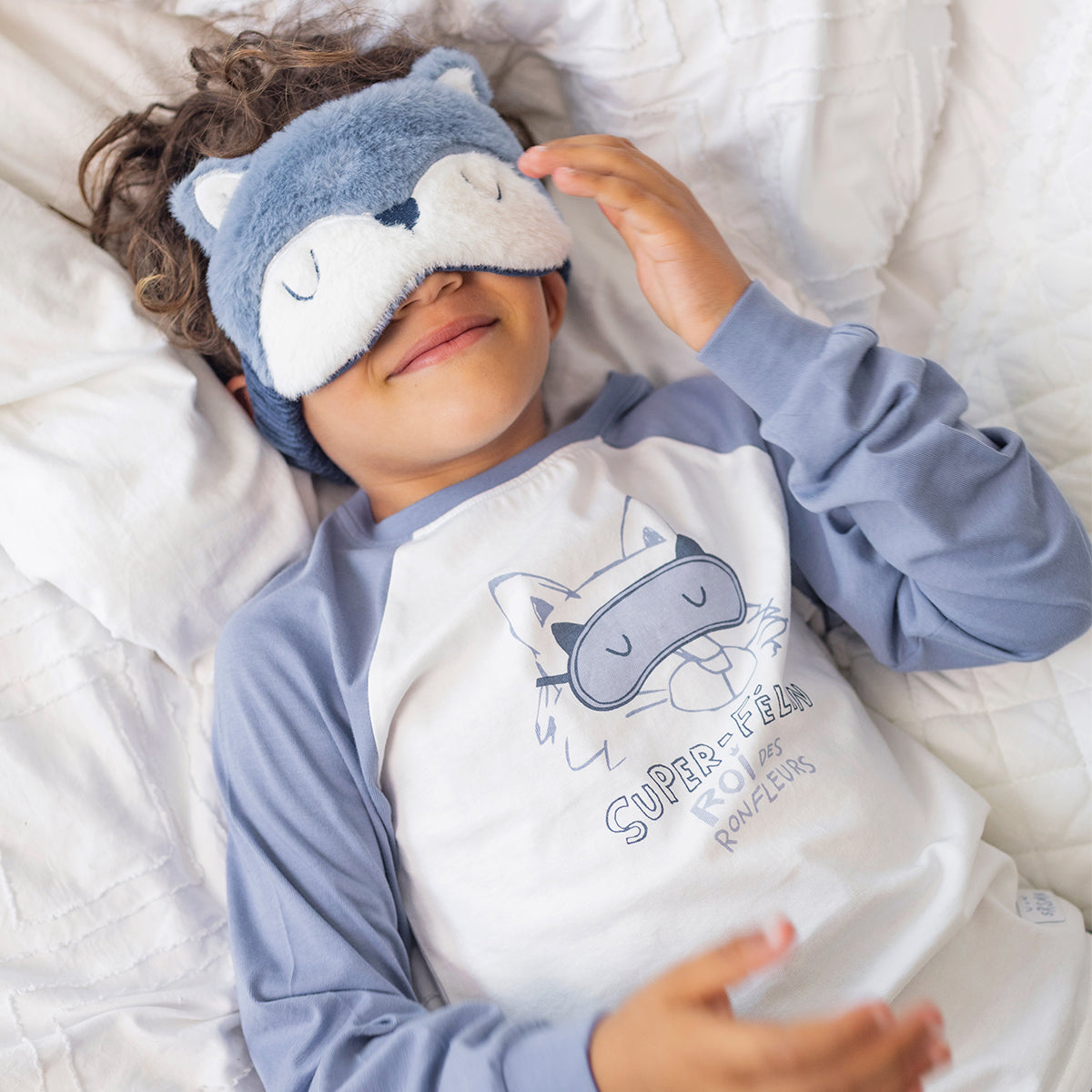 Enfant portant le pyjama deux pièces bleu à illustration de chat en coton doux, allongé sur un lit avec un masque de sommeil en forme de chat assorti