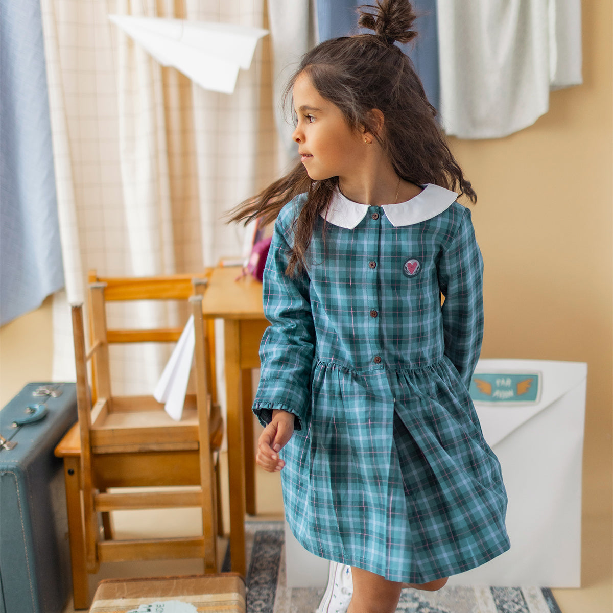 Robe turquoise à carreaux en flanelle pour enfant avec col blanc, manches longues, boutons effet bois et écusson cœur brodé, portée par une enfant.