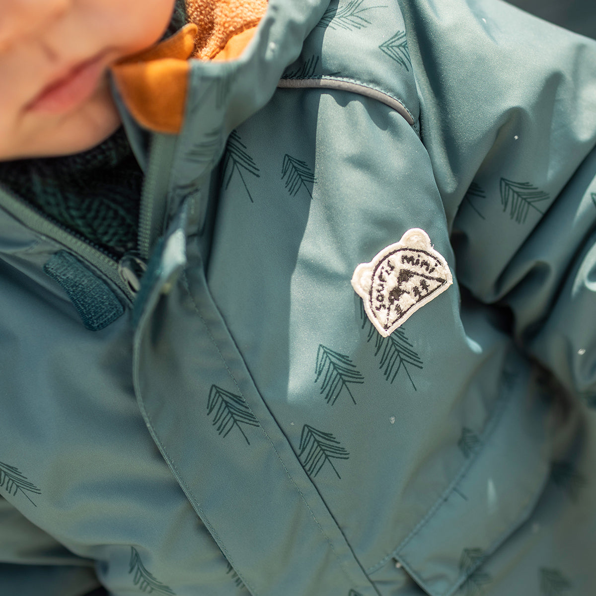 Photo d'un bébé portant l'habit de neige deux pièces vert avec motifs de sapins, bébé