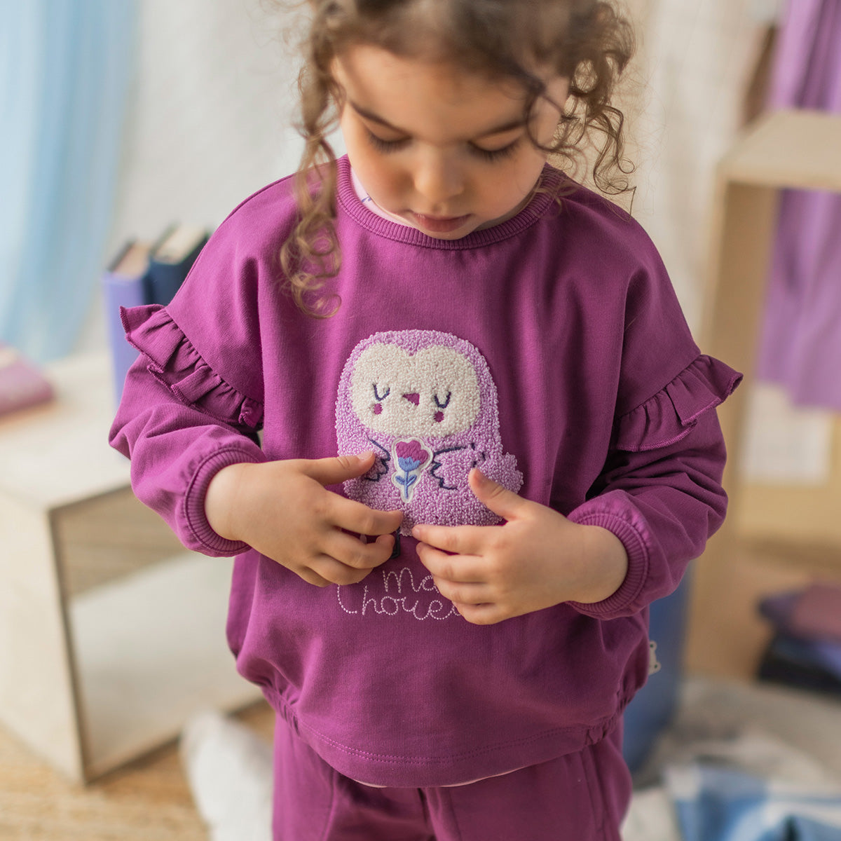 Chandail mauve en coton français pour bébé avec illustration texturée d'une chouette sur le devant et manches longues à volants, porté par un bébé.