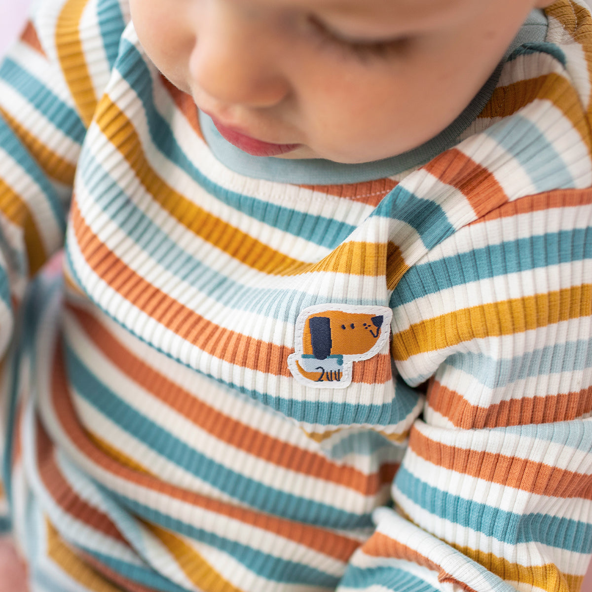 Pyjama deux pièces rayé crème, bleu et orangé pour bébé en coton côtelé, porté par un bébé et orné d'un écusson de chien