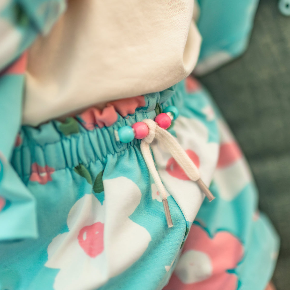 Zoom breloques sur l'attache à la taille du short bleu aqua à motif floral, bébé