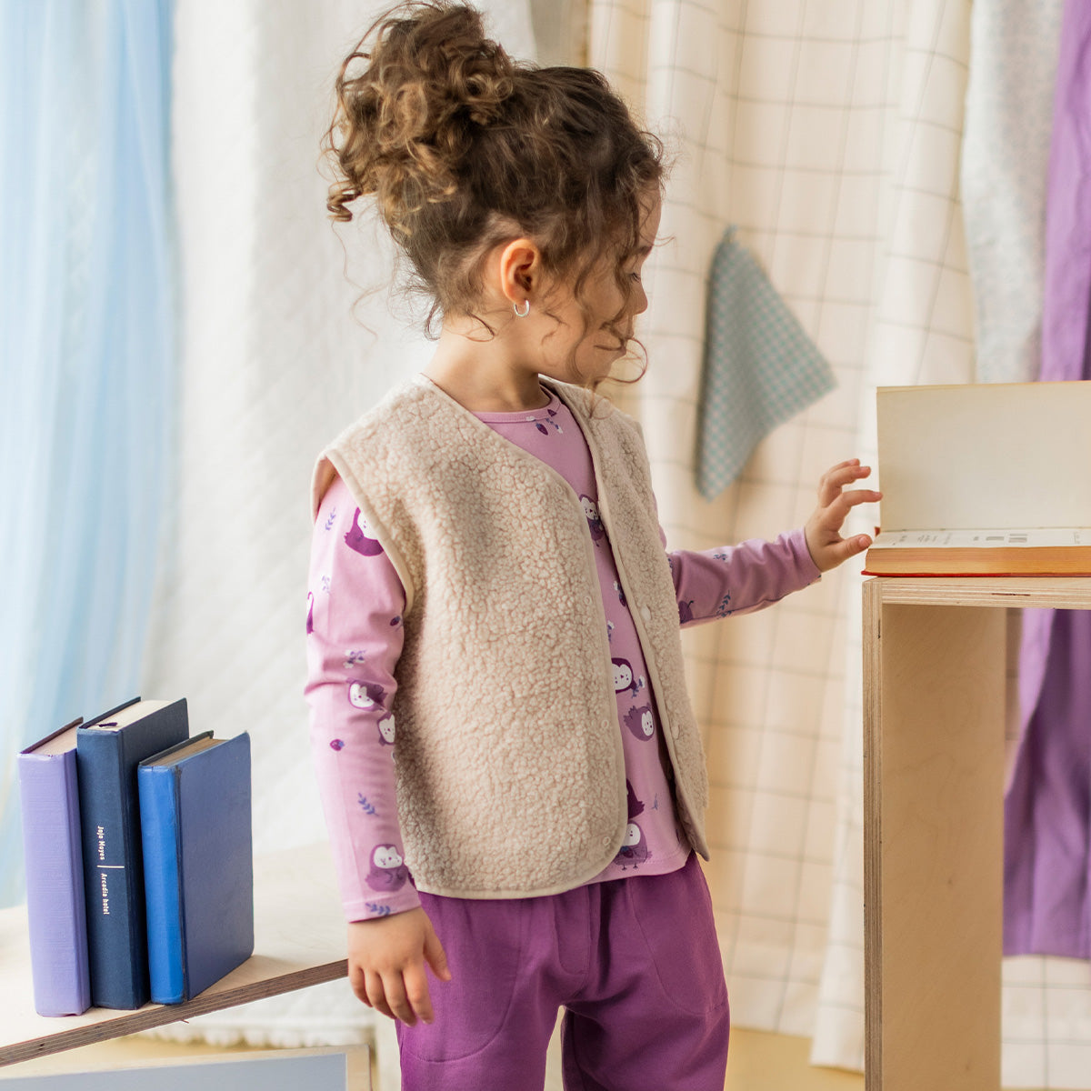 T-shirt mauve à imprimé de chouettes pour bébé à manches longues, porté sous une veste sans manches en sherpa.