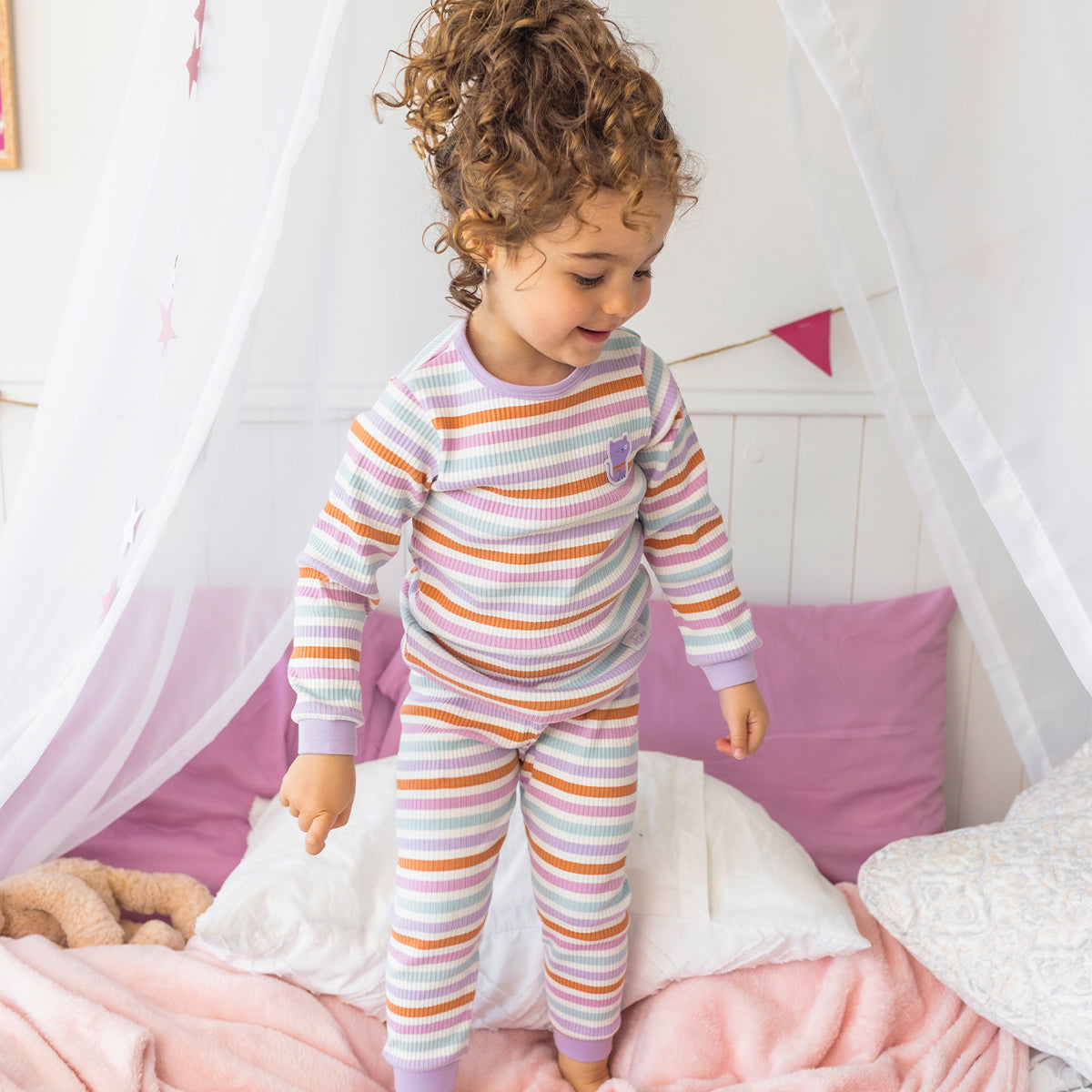 Pyjama deux pièces rayé multicolore pour bébé en coton côtelé, porté par un bébé dans une chambre