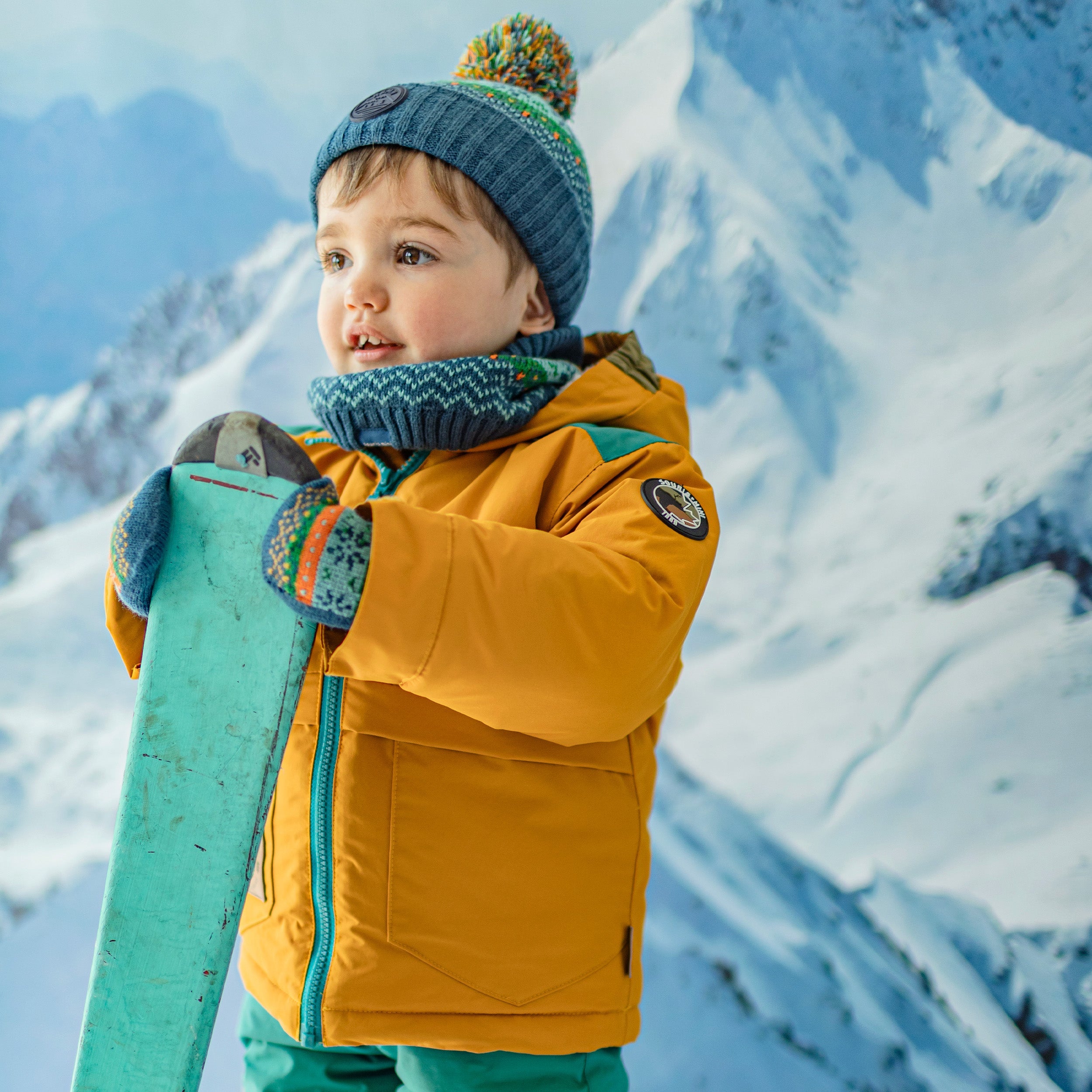 Photo d'un enfant portant les mitaines bleues, vertes, orange et turquoise à motifs avec cordon en tricot, bébé