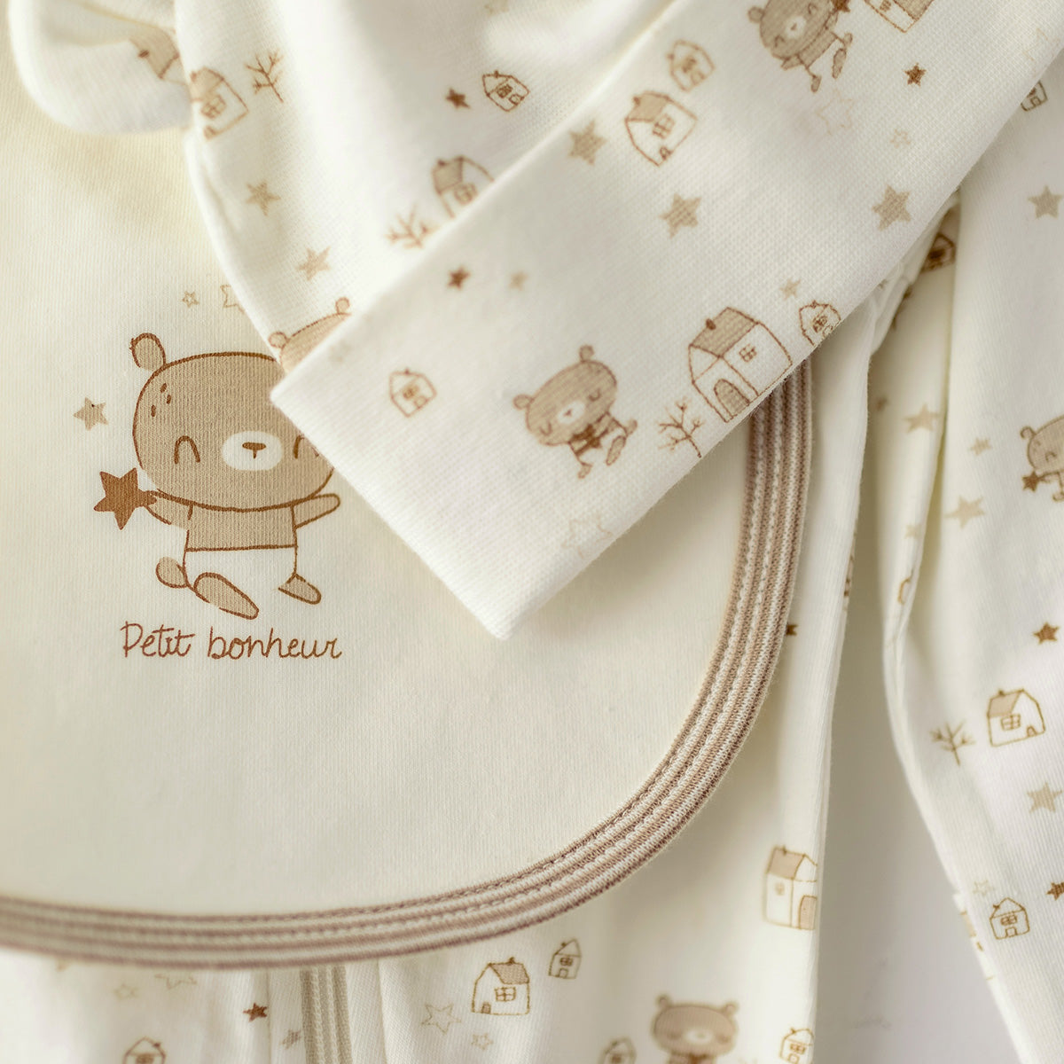 Zoom détails de l’ensemble pyjama, bavoir et chapeau crème et beige, naissance