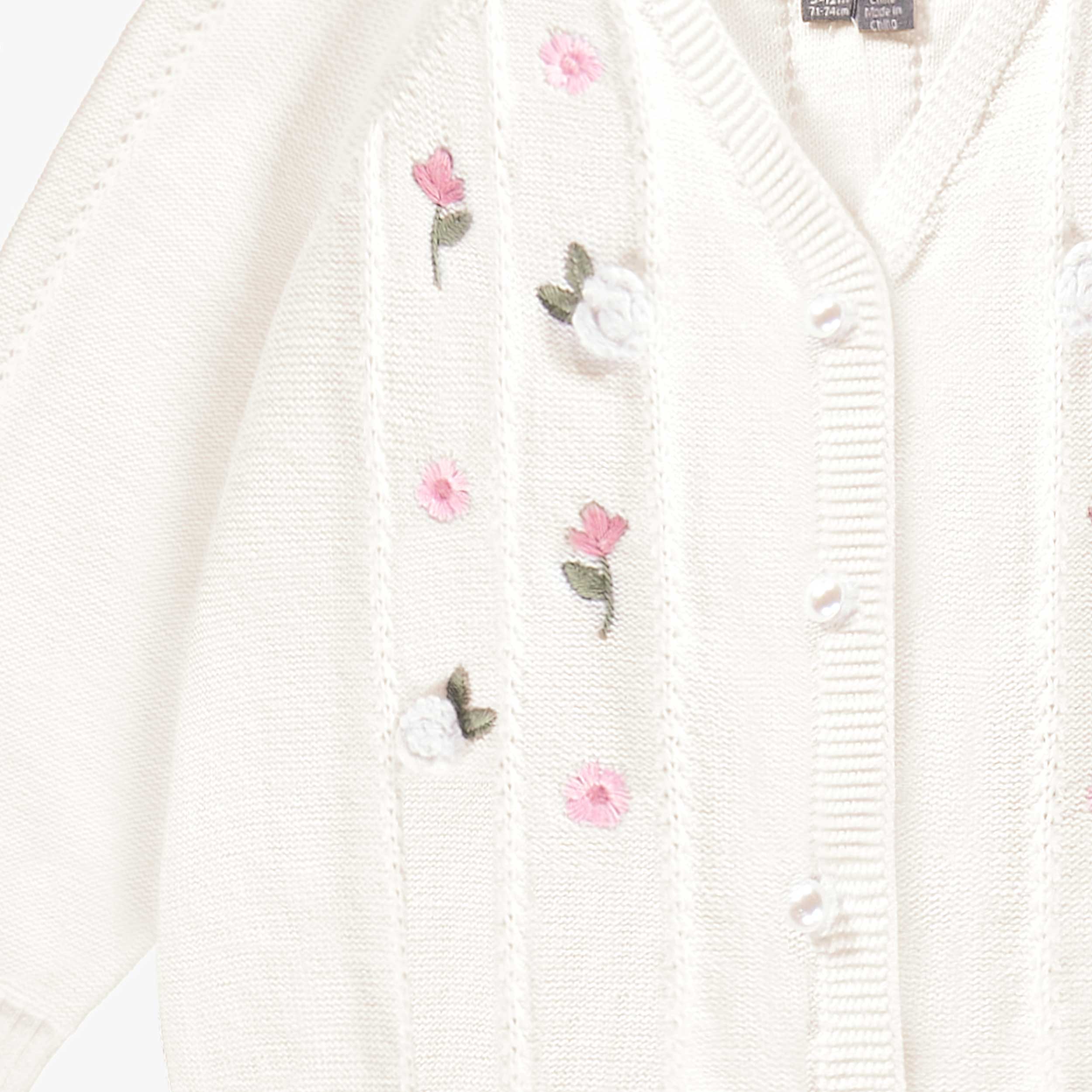 Détail du cardigan blanc en tricot avec détails ajourés et fleurs crochetées, bébé