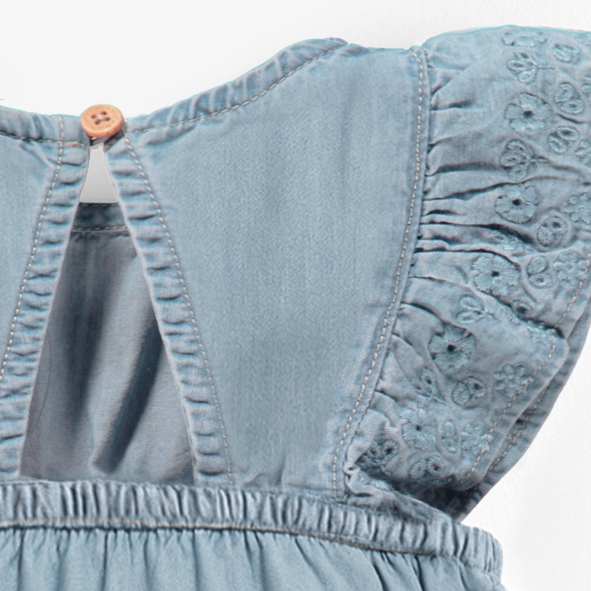 Zoom détails dos de la barboteuse bleu pâle en denim avec broderie anglaise, naissance