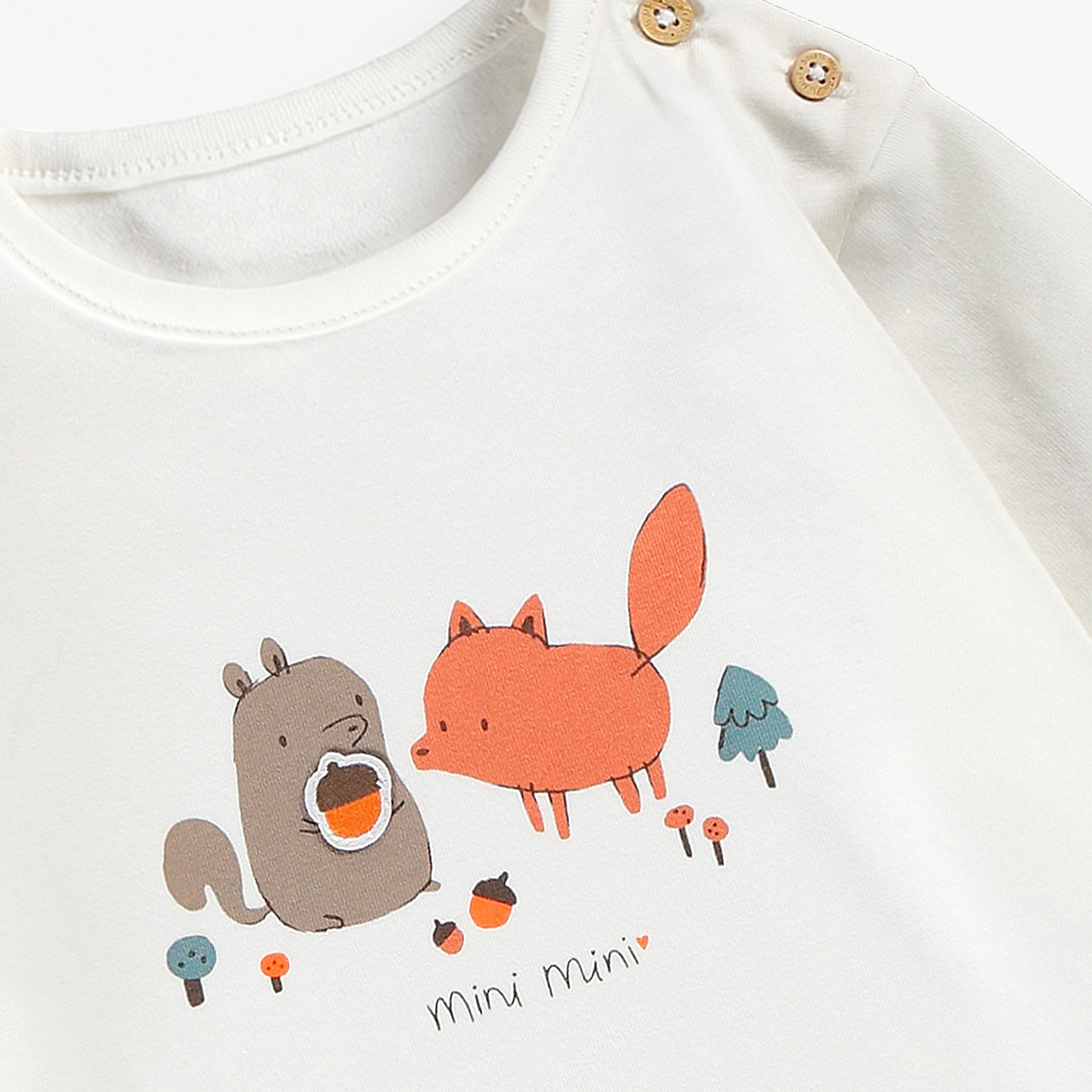 Gros plan sur le chandail blanc pour bebe garcon avec boutons decoratifs a l'epaule et illustration d'un renard et d'un raton laveur sur le devant.