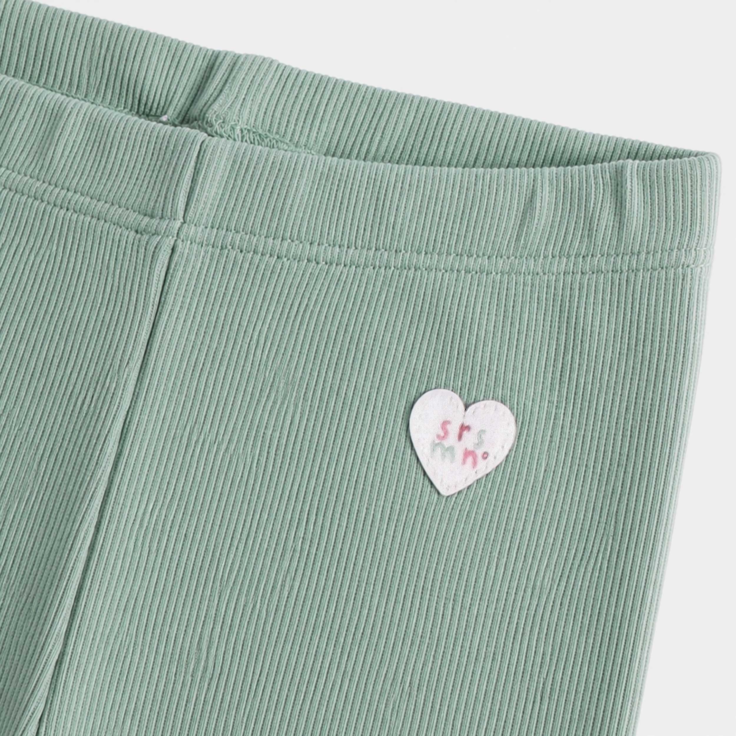 Gros plan sur un legging vert sauge pour bébé fille en tissu côtelé extensible, avec taille élastique confortable et écusson cœur décoratif.