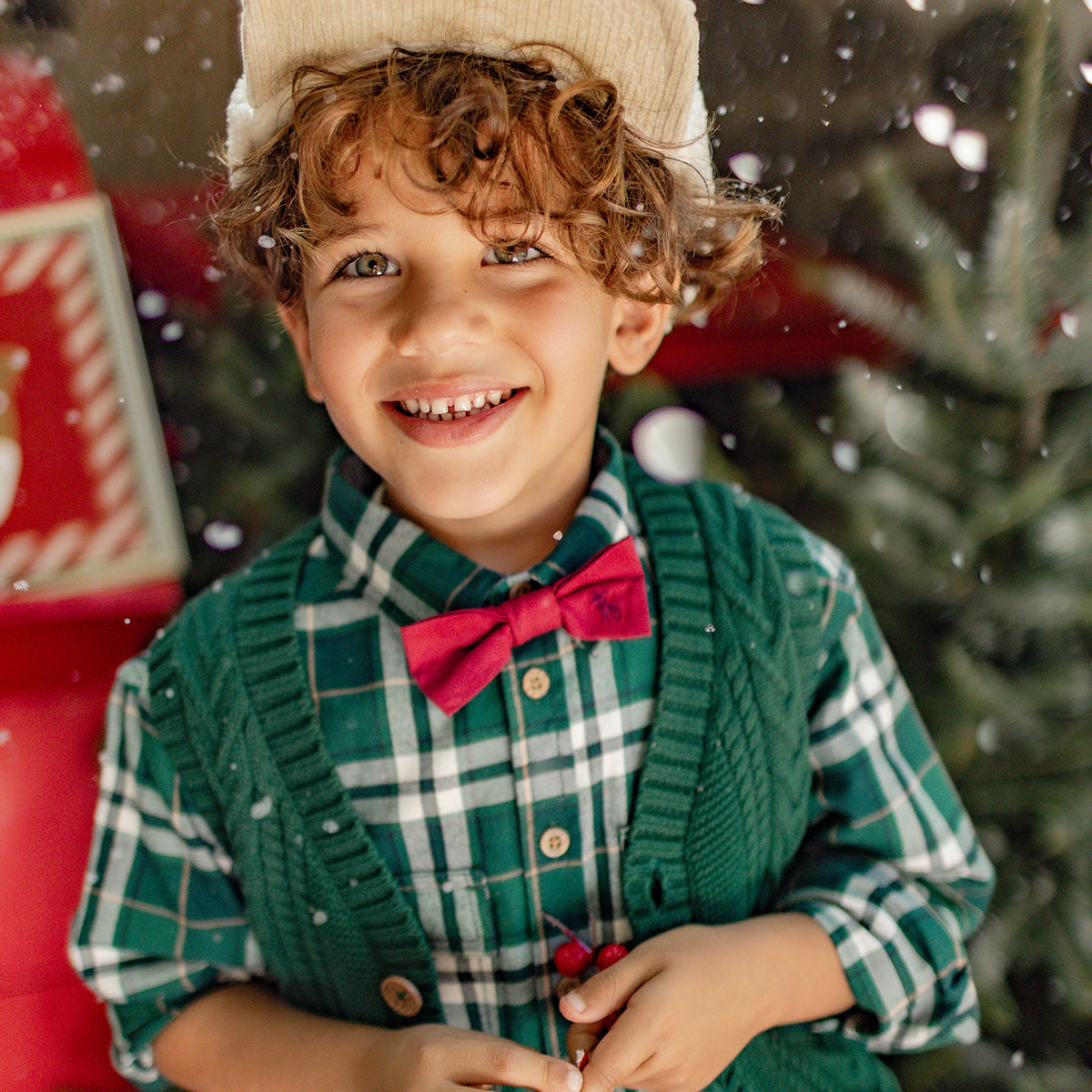 Petit garçon souriant portant une chemise verte à carreaux, et un nœud papillon, parfait pour un look chic des Fêtes.