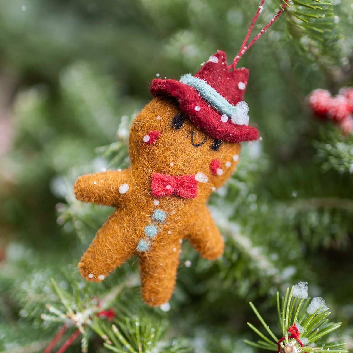 Décoration de Noël Souris Mini en feutre représentant un bonhomme en pain d’épice avec chapeau rouge et nœud papillon sur un sapin enneigé.