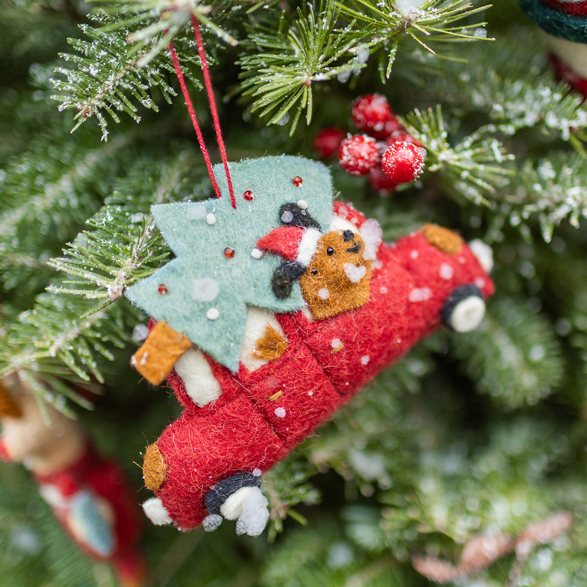 Décoration de Noël Souris Mini en feutre représentant une voiture rouge avec un ourson et un sapin, suspendue dans le sapin enneigé.