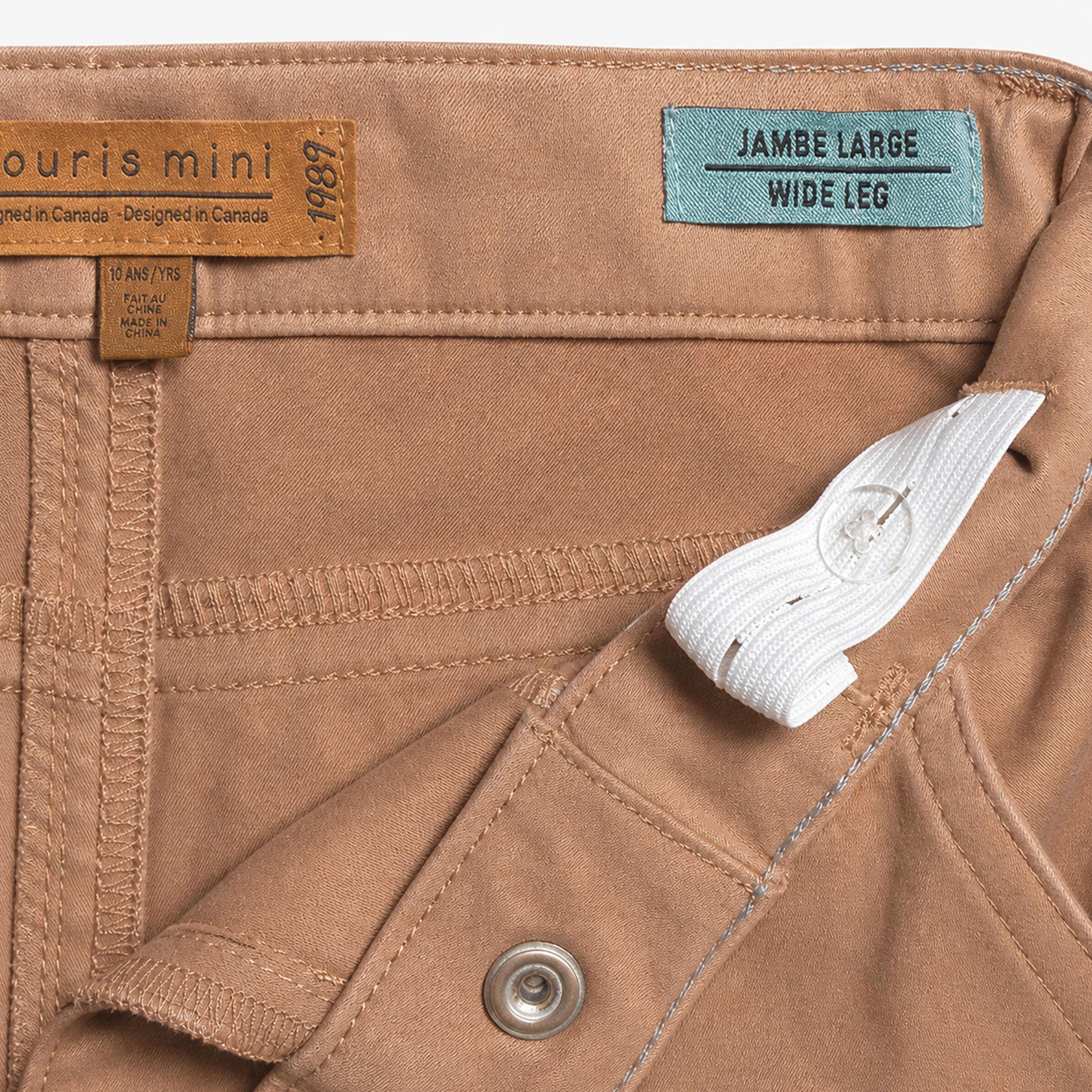Gros plan sur l’intérieur de la ceinture ajustable d’un pantalon enfant beige camel à coupe jambe large.