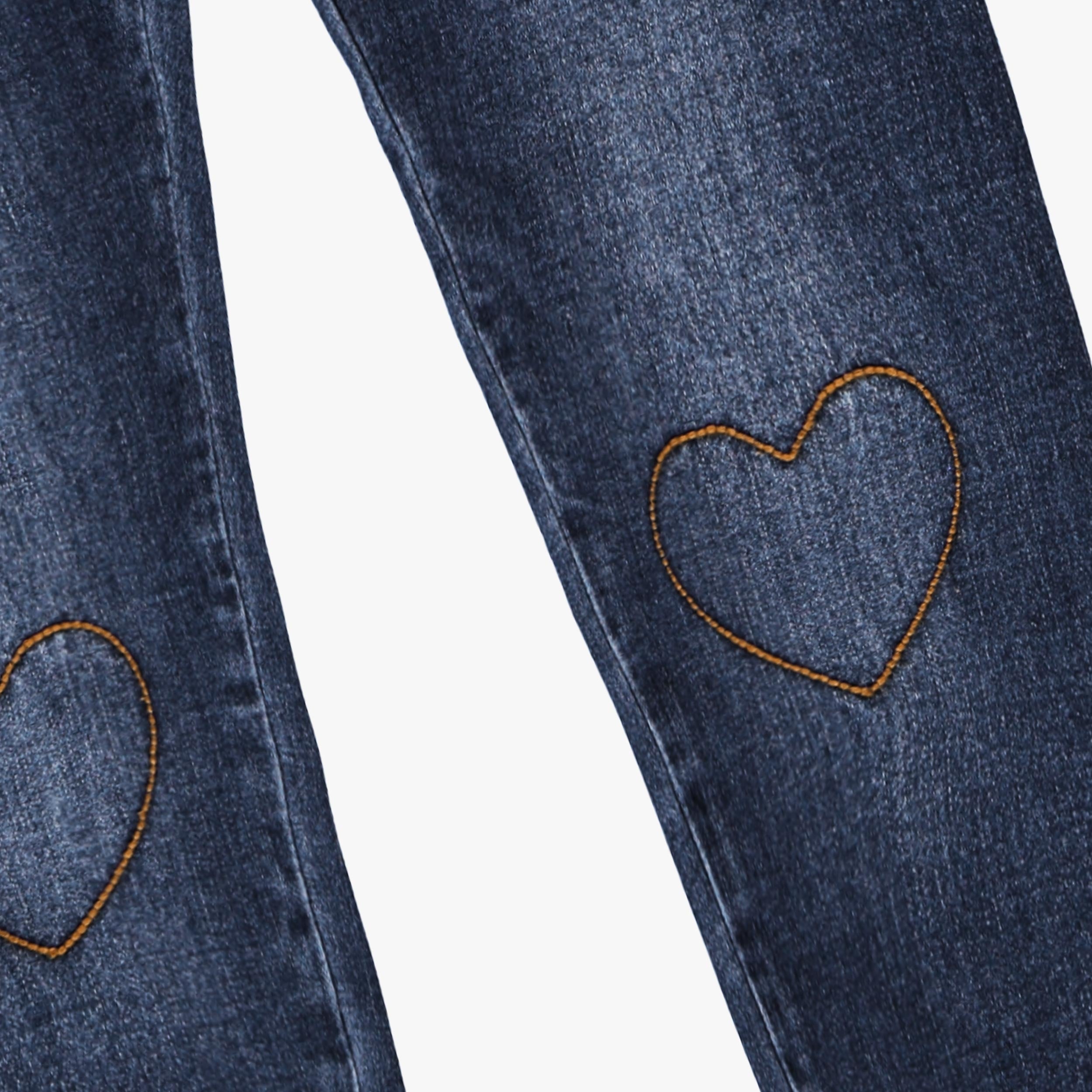 Gros plan sur une broderie en forme de cœur sur un jean enfant fille en denim bleu foncé délavé.