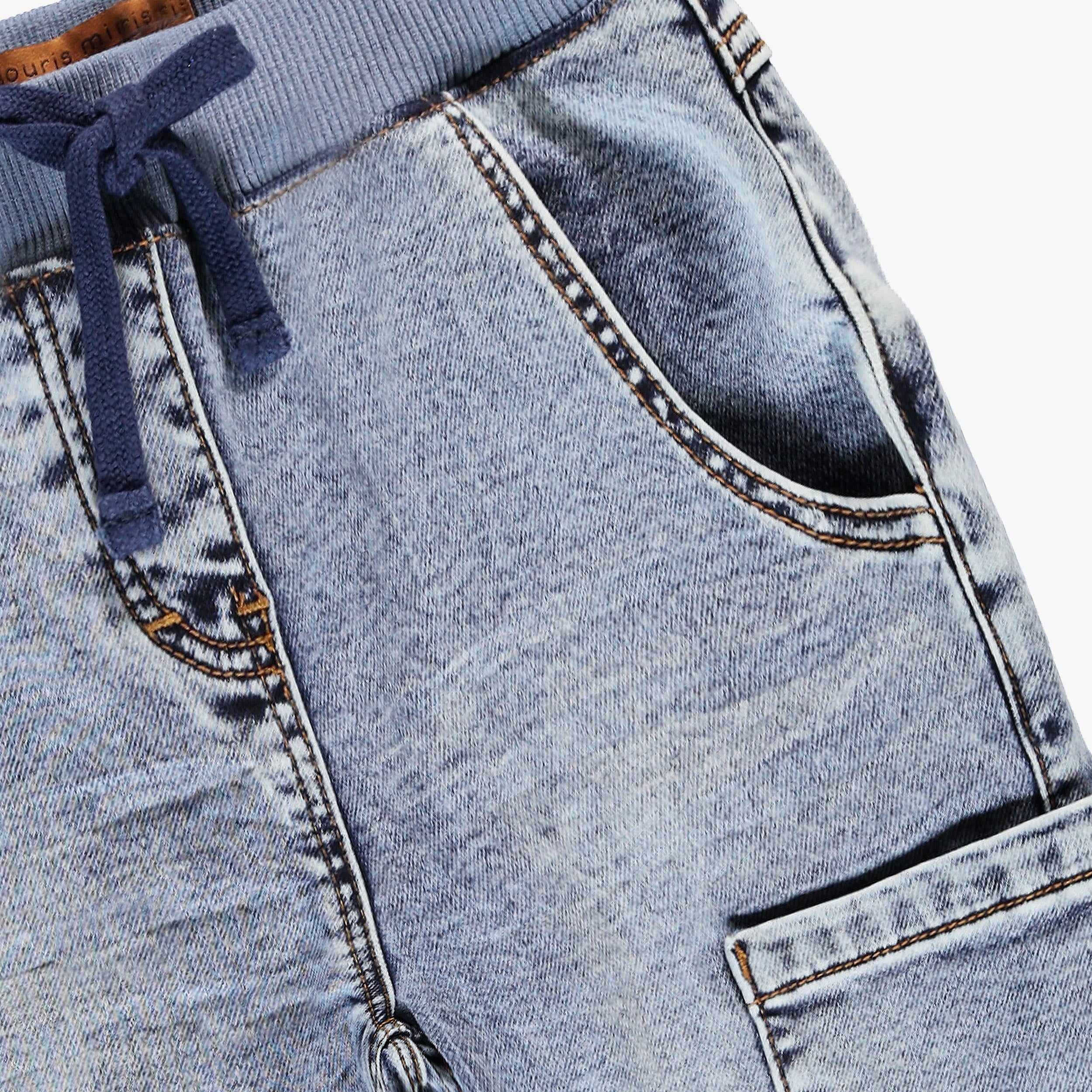 Gros plan sur la taille élastiquée à cordon et les poches avant d’un pantalon jogger enfant en jean bleu clair délavé.
