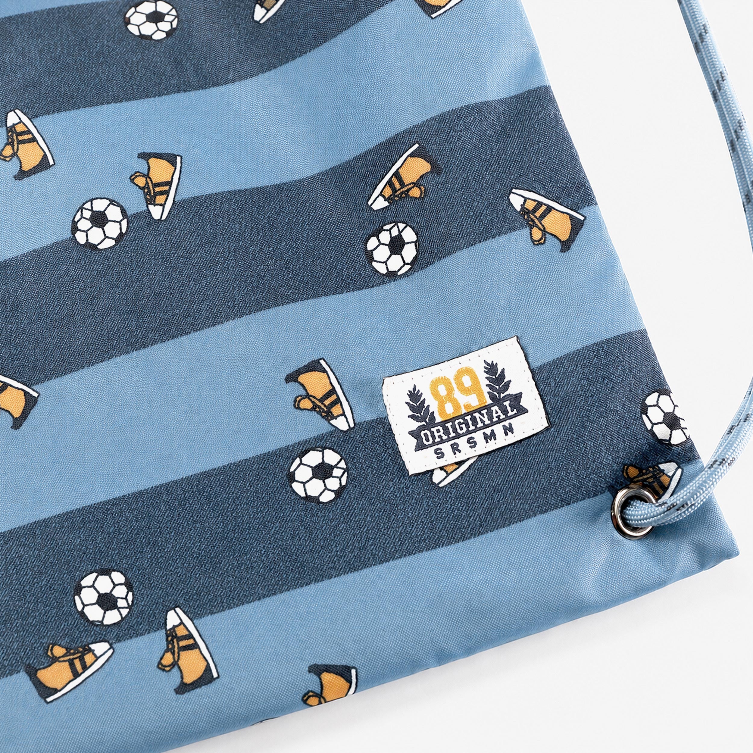 Zoom sur le tissu d’un sac de gym enfant bleu avec motif football, ballons de soccer et chaussures de sport.