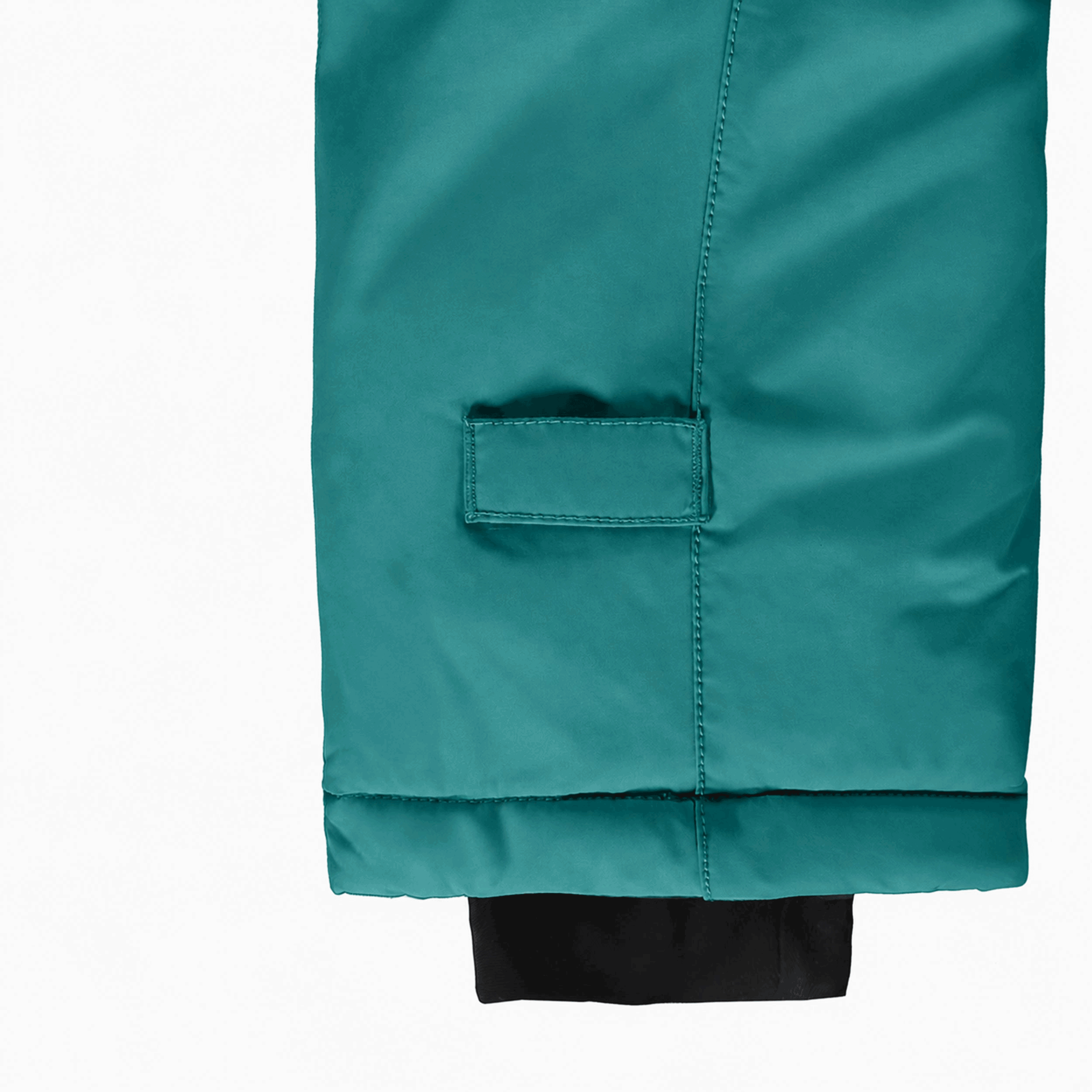 Gros plan sur la jambe d’une combinaison de neige pour bébé turquoise montrant l’ourlet ajustable évolutif et le poignet intérieur coupe-froid.