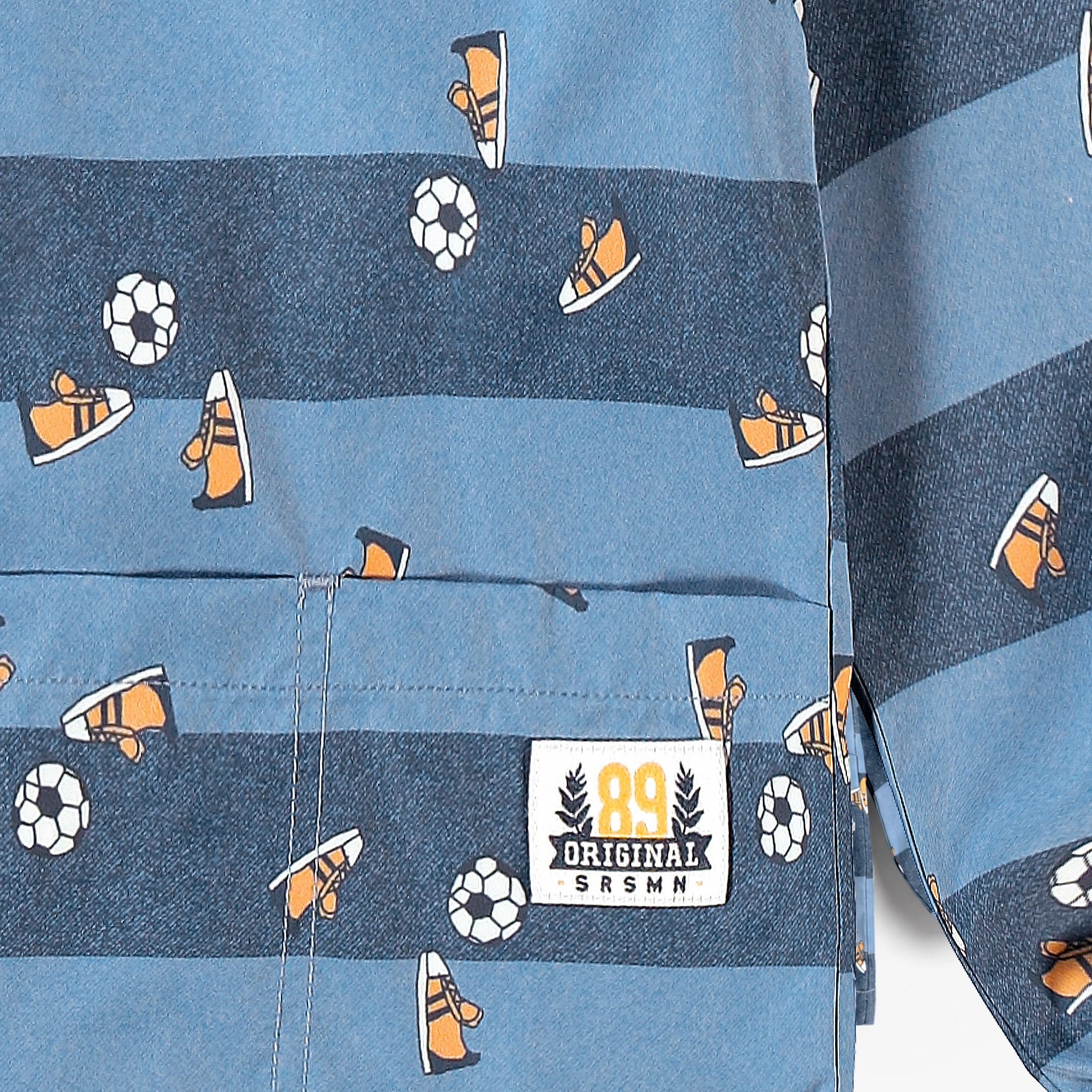 Gros plan sur le tissu d’un tablier enfant bleu à rayures avec motifs football, baskets et poche avant.