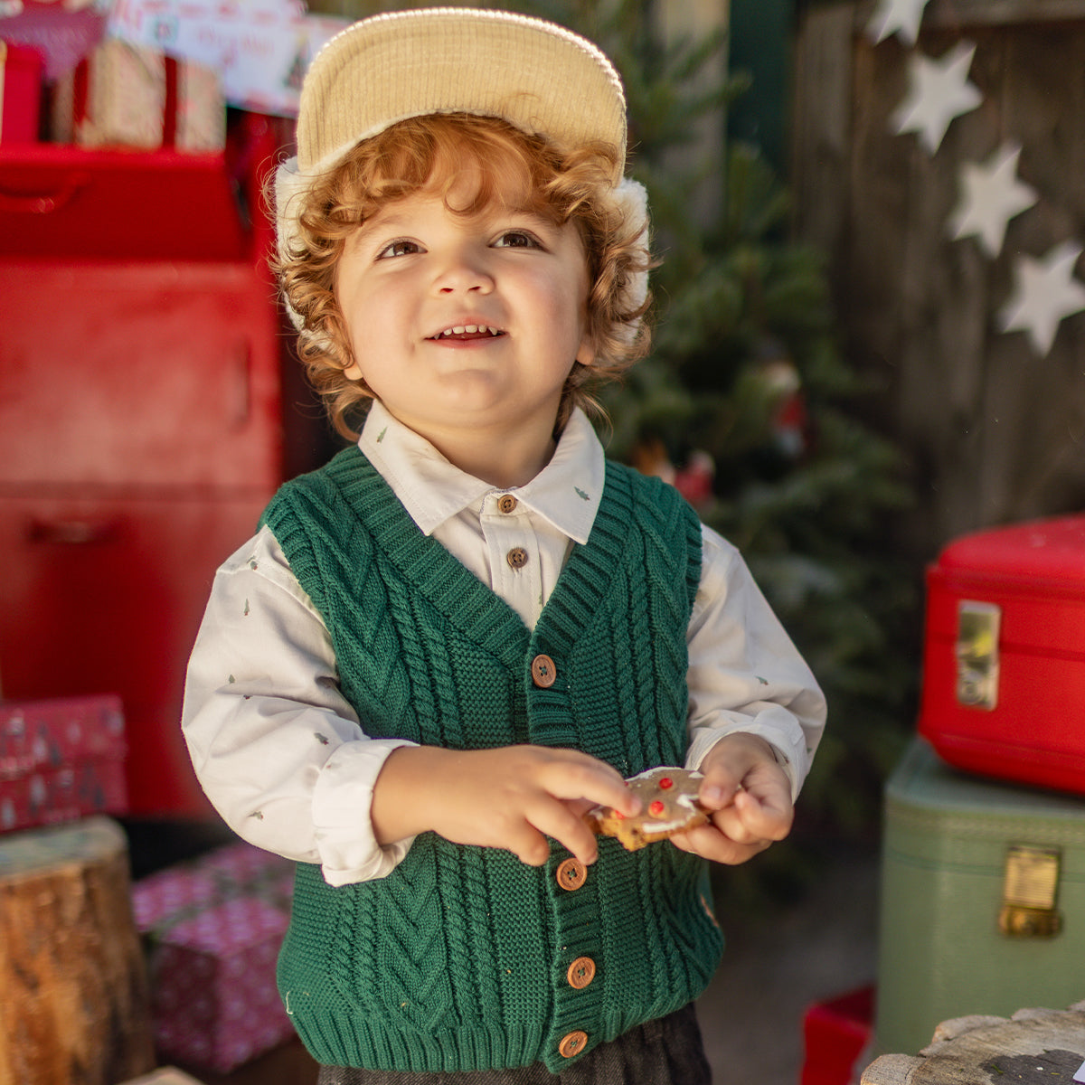 Petit garçon portant un gilet tricoté vert et une chemise blanche à motifs, tenant un biscuit de Noël, collection festive Souris Mini.