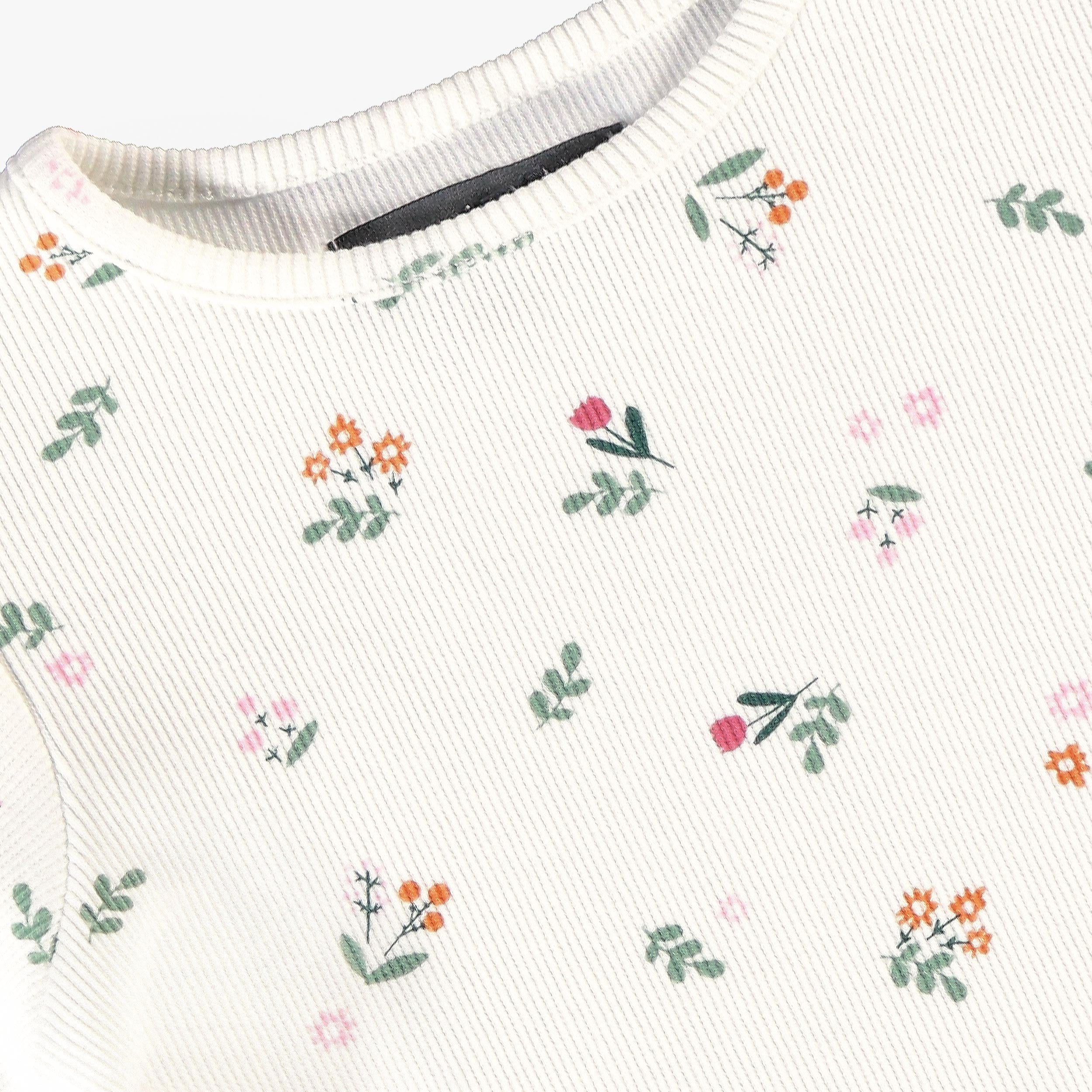 Détail du haut bébé écru en maille côtelée avec imprimé petites fleurs