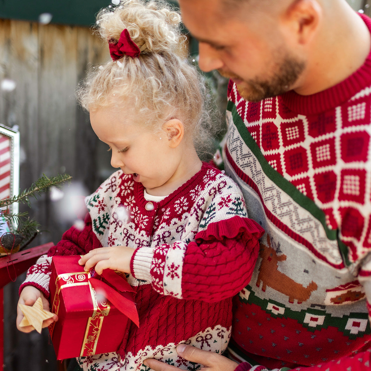Père et fille portant des chandails rouges en tricot à motifs festifs de Noël, partageant un moment complice en ouvrant un cadeau, collection des Fêtes Souris Mini.