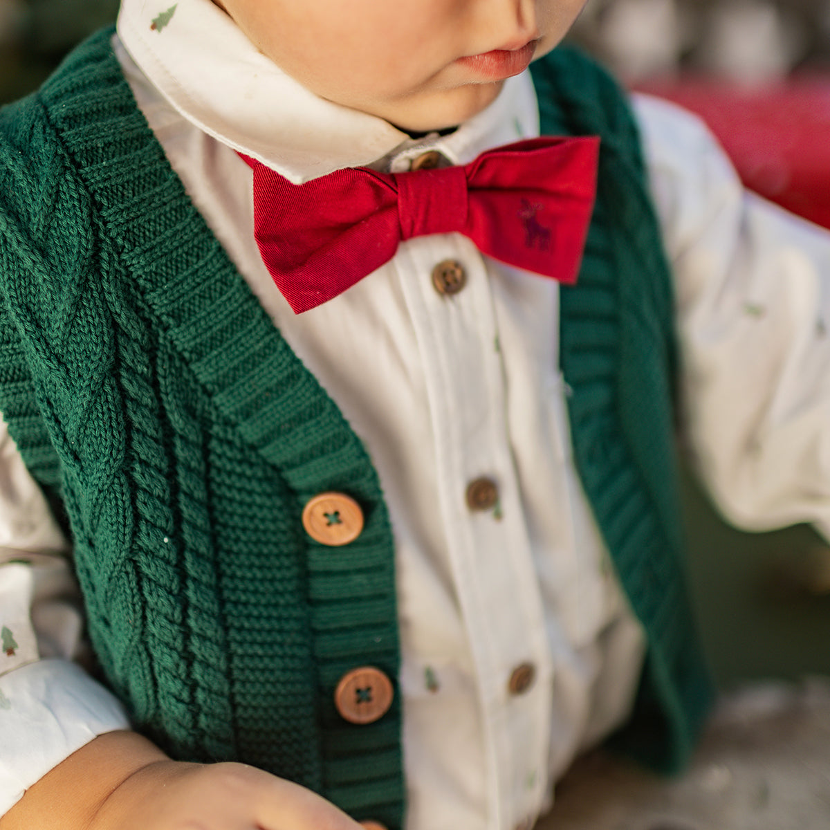 Gros plan sur un enfant portant un nœud papillon rouge, une chemise blanche à motifs et un gilet tricoté vert, tenue de Noël Souris Mini.