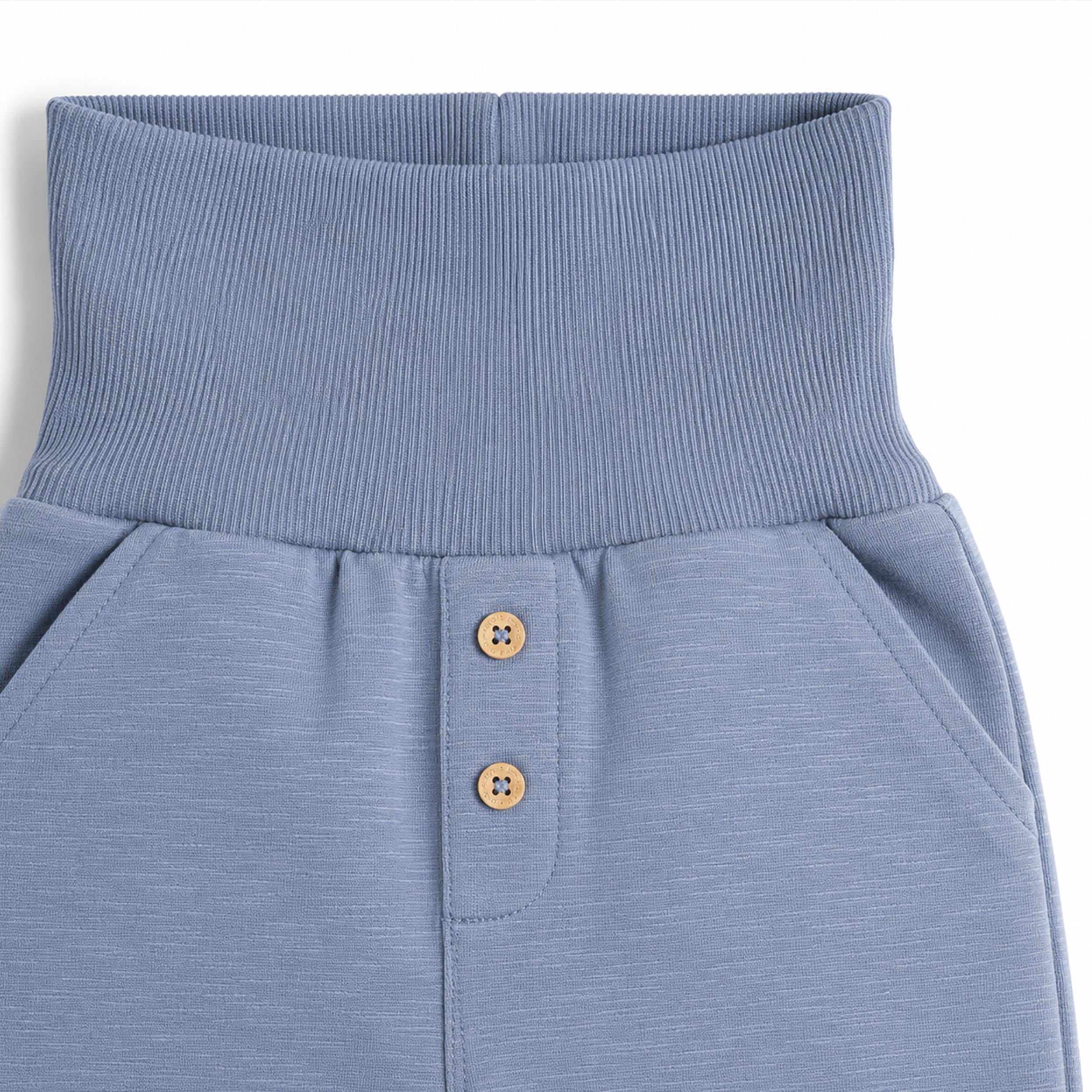 Zoom sur la taille élastique et les boutons décoratifs d’un pantalon bébé bleu clair