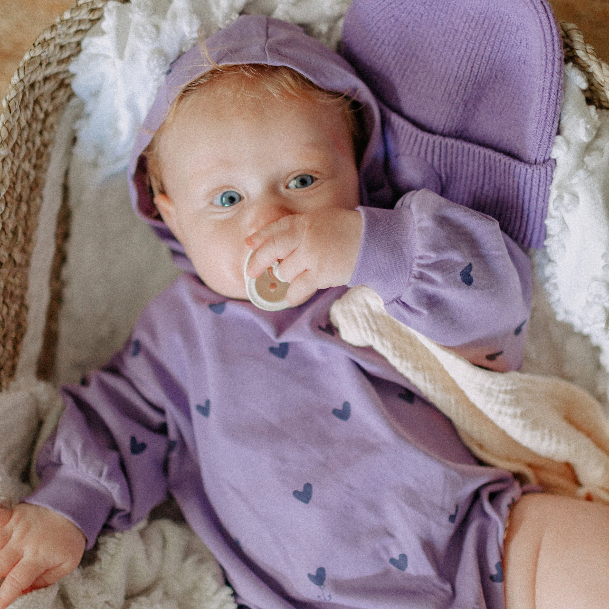 Photo d'un bébé portant l'une-pièce mauve à capuchon avec motifs de cœur en doux jersey de coton biologique, naissance