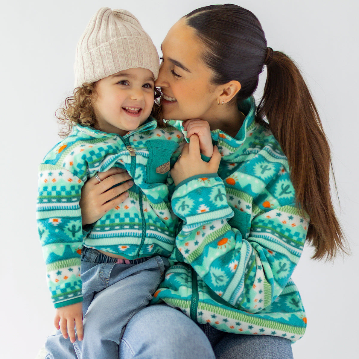 Parent embrassant un enfant portant des polaires assorties turquoise à motifs Souris Mini, dans un moment tendre et complice.