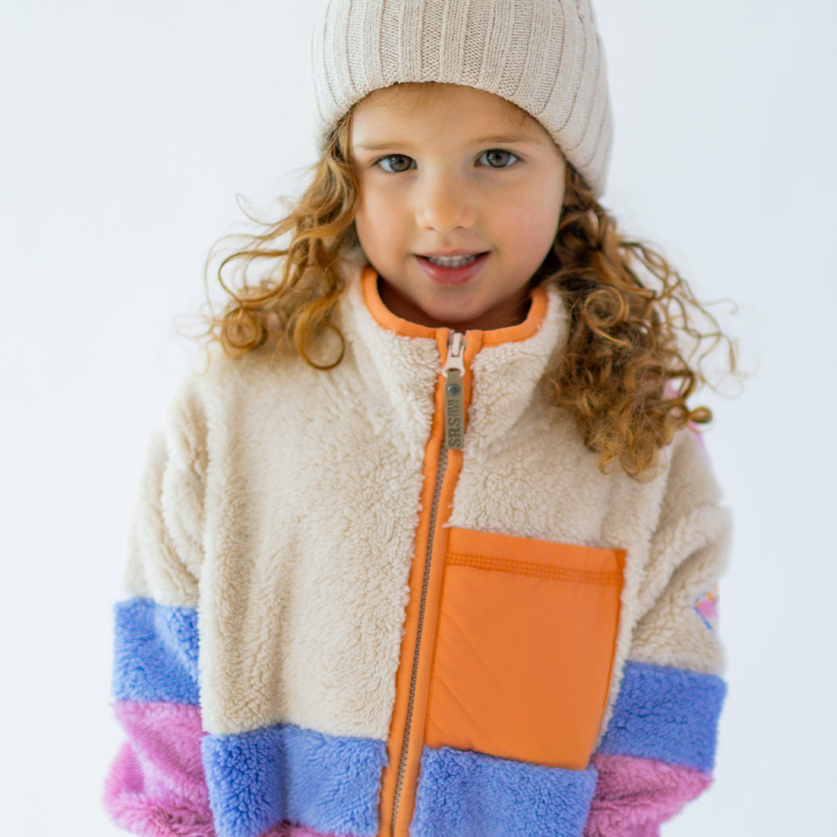 Portrait d’une enfant portant une polaire Souris Mini crème, mauve et rose avec poche poitrine orange.
