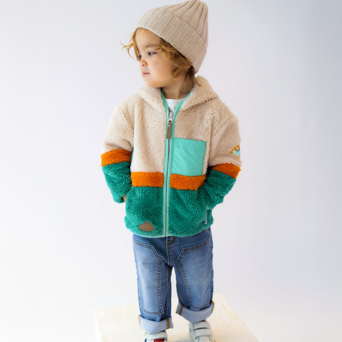 Enfant portant une polaire Souris Mini multicolore vert, beige et orange avec fermeture éclair et poche poitrine.