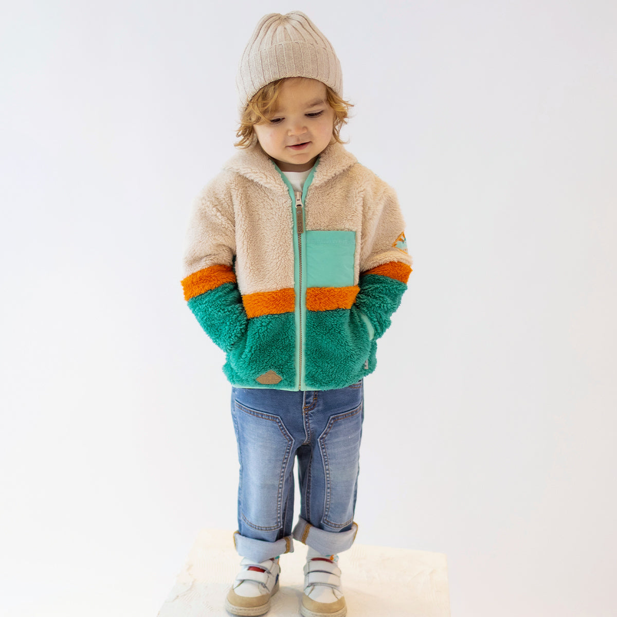 Enfant portant une polaire Souris Mini vert, beige et orange avec fermeture éclair et poche poitrine, vue de face.