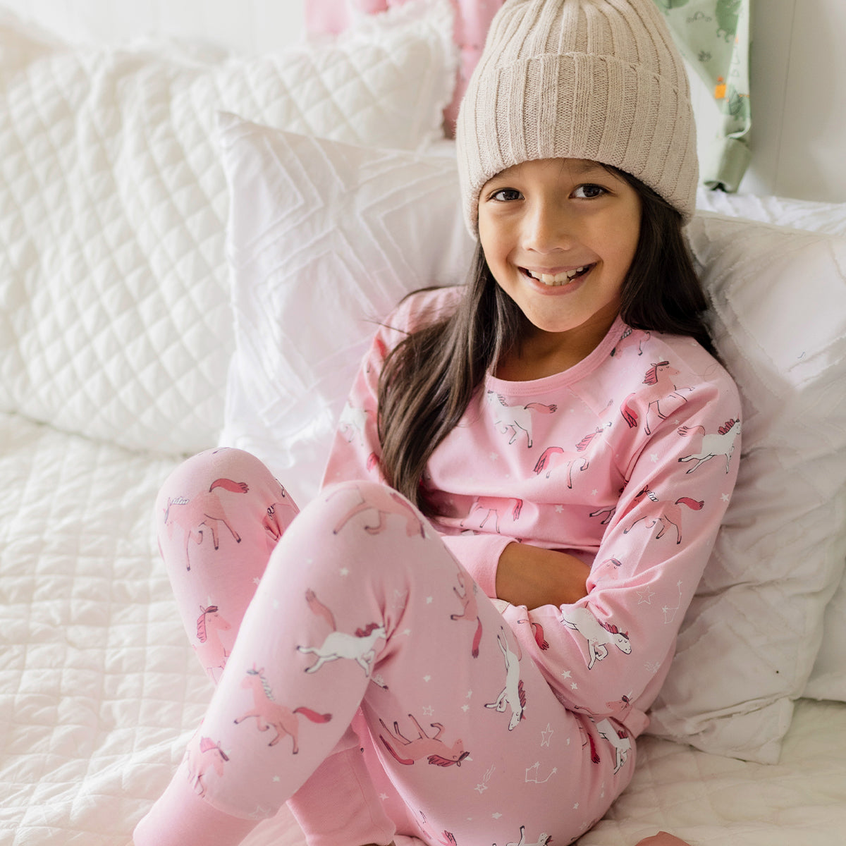 Fille portant un pyjama rose en coton à motifs de licornes Souris Mini, confortablement assise sur un lit douillet.