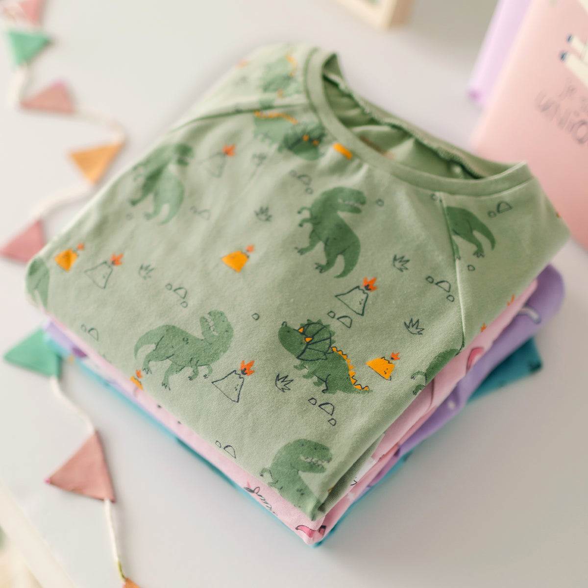 Pile de pyjamas Souris Mini pour enfants, avec un modèle vert à dinosaures au-dessus et des modèles licorne et dragon en dessous.