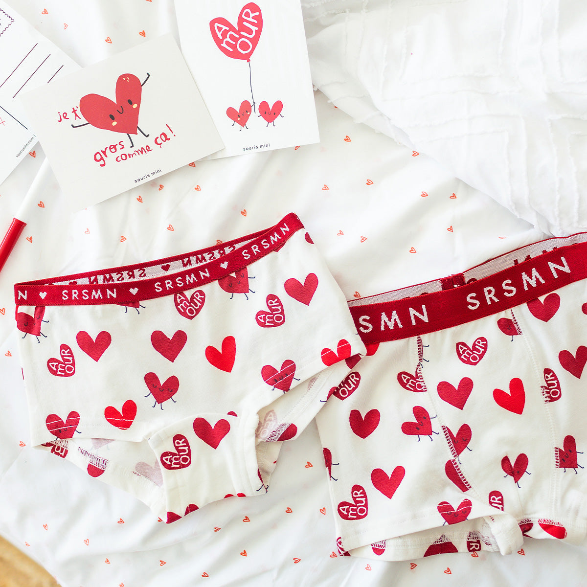 Sous-vêtements enfants Souris Mini à motifs de cœurs rouges, présentés à plat sur un lit avec cartes assorties.