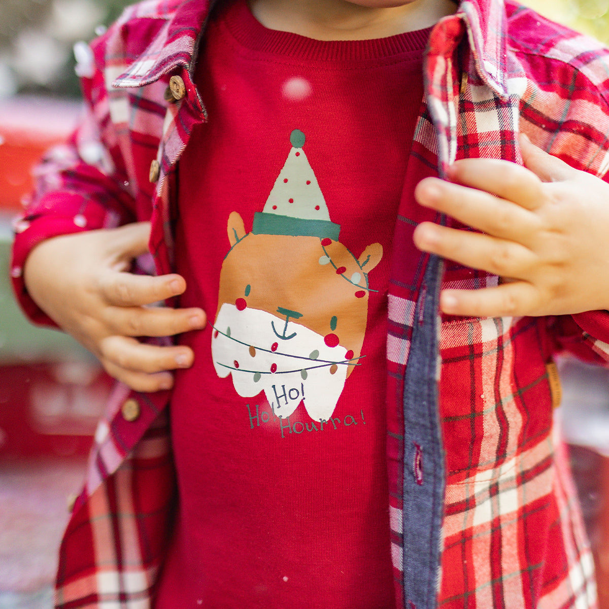 Gros plan sur un t-shirt rouge pour enfant avec imprimé d’ours de Noël et guirlande lumineuse, porté sous une chemise à carreaux, collection Souris Mini.