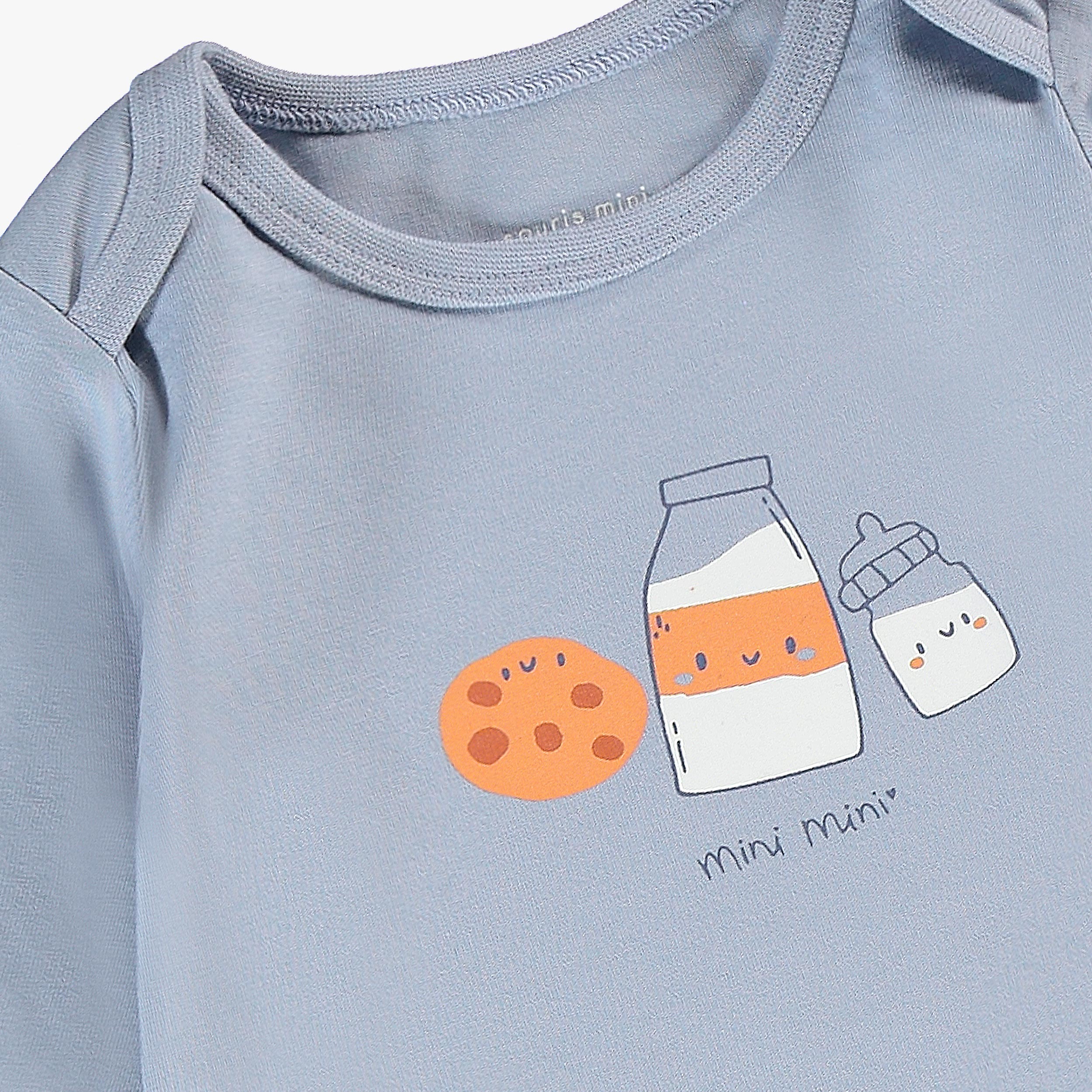 Zoom sur l’illustration de biscuit et bouteilles de lait du cache-couche bébé bleu en coton.