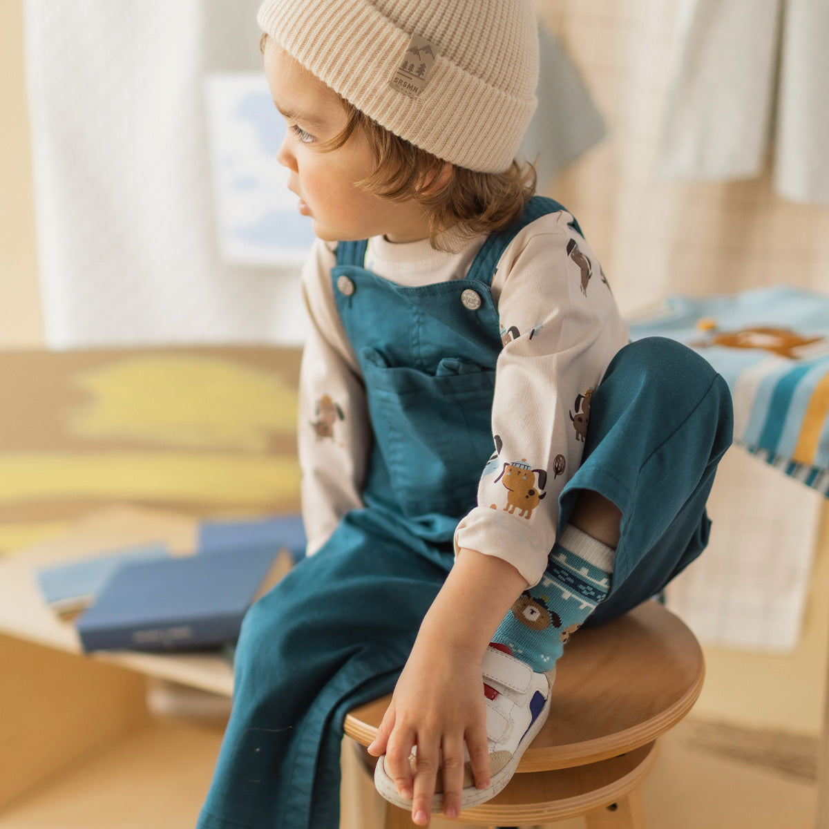 T-shirt crème à imprimé de chiens pour bébé à manches longues, porté sous une salopette vert foncé en denim.