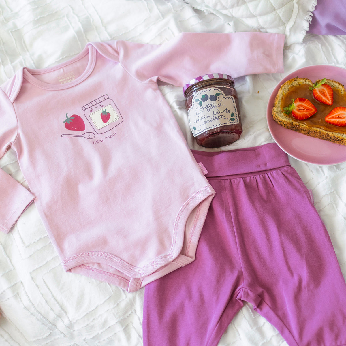 Cache-couche rose à illustration pour bébé en coton doux, avec motif de fraise et pot de confiture, présenté avec un pantalon mauve assorti