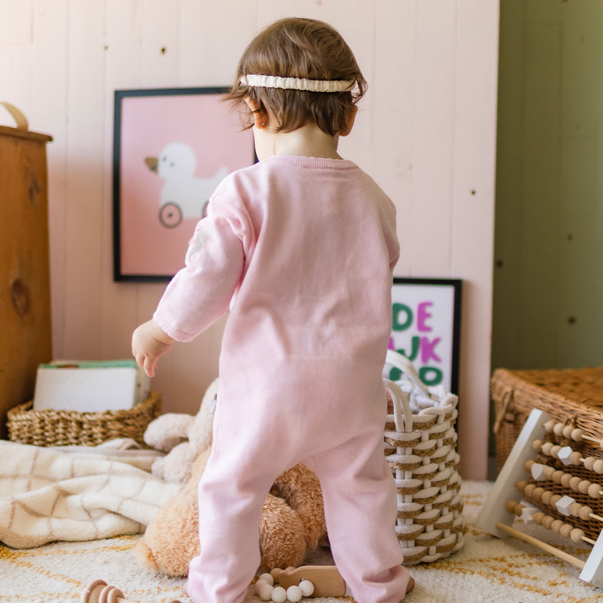 Photo d'un enfant de dos portant le une pièce rose en tricot avec motifs, naissance