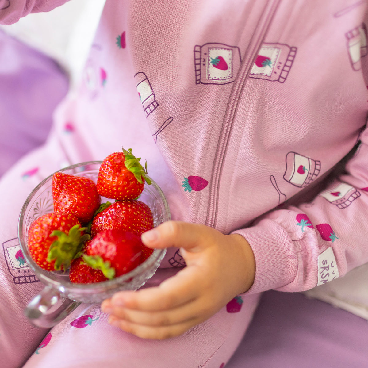 Gros plan du pyjama une pièce mauve à petits motifs pour bébé en coton doux, avec fermeture éclair et imprimé de fraises et pots de confiture.