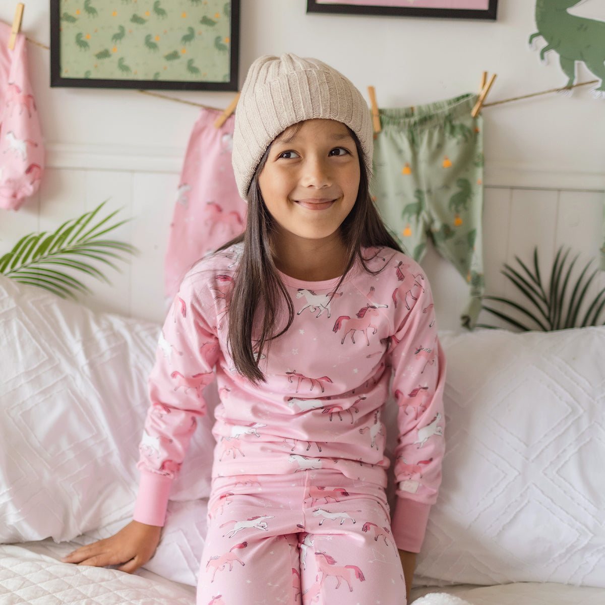 Fille portant un pyjama rose en coton à motifs de licornes Souris Mini, confortablement assise sur un lit douillet.