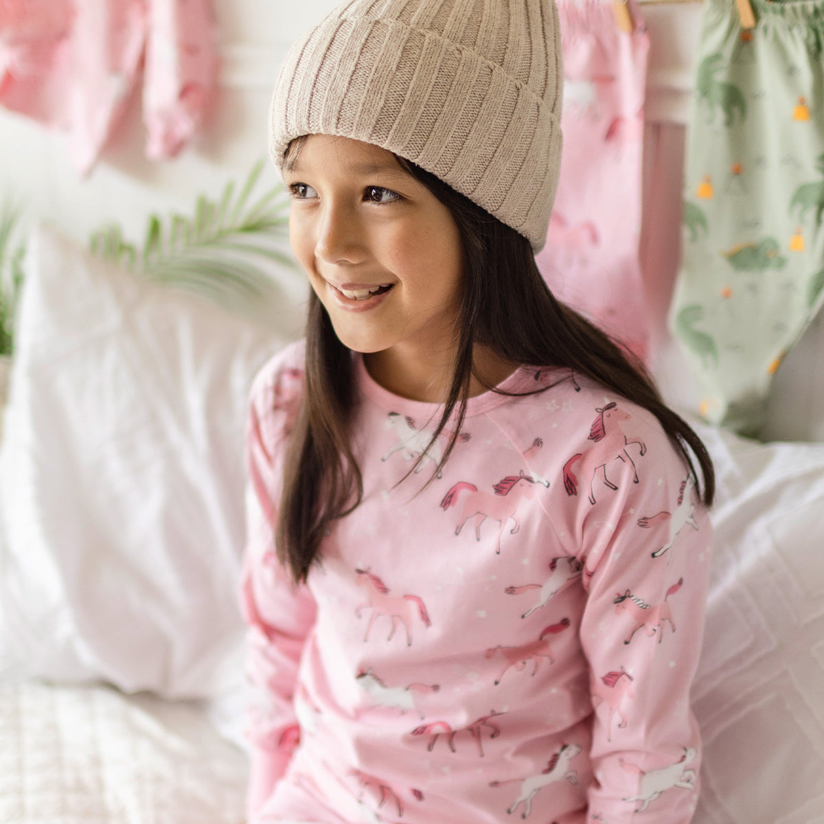 Fille portant un pyjama rose en coton à motifs de licornes Souris Mini, confortablement assise sur un lit douillet.