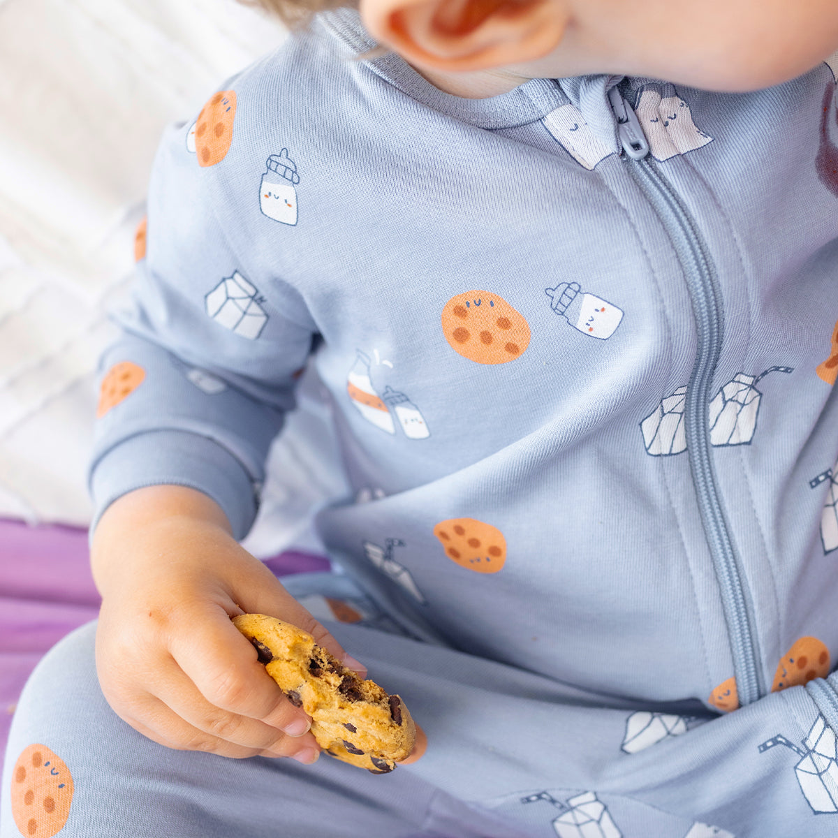 Gros plan du pyjama une pièce bleu à petits motifs pour bébé en coton doux, avec fermeture éclair et imprimés de biscuits, briques de lait et biberons