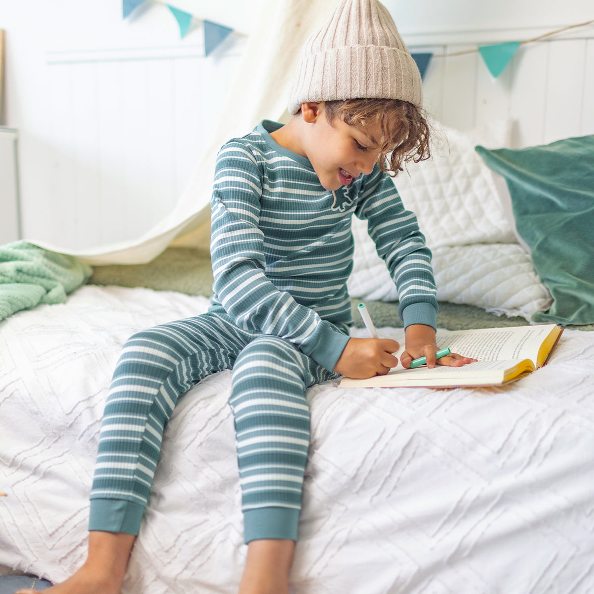 Enfant portant le pyjama deux pièces vert à rayures en coton côtelé, assis sur un lit